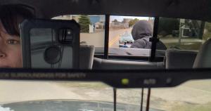 Camera mounted on back of truck filming characters driving in a car seen through a rearview mirror.